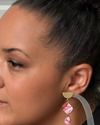 A close-up side profile of a woman wearing a gold and pink drop earring.