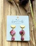 A pair of handmade dangle earrings with gold-tone semicircle studs and pink marbled stone drops.