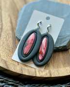 A pair of oval drop earrings with black outer frames and inset pink marbled faux stone centers