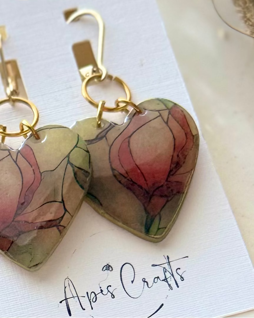 Heart-shaped dangling earrings with a watercolor-style floral design in muted pink, green, and beige tones
