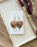 A pair of heart-shaped dangling earrings with a floral pattern in amber, purple, and green