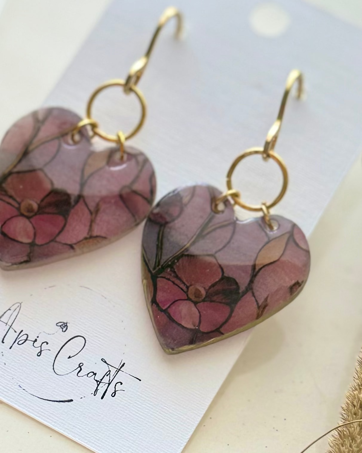 A pair of heart-shaped dangling earrings with a floral pattern in pink, purple, and green