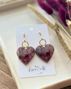 A pair of heart-shaped dangling earrings with a floral pattern in pink, purple, and green