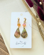 A pair of teardrop-shaped drop earrings with gold-tone hooks and orange crysta, featuring marbled green, beige, and brown stained glass drops