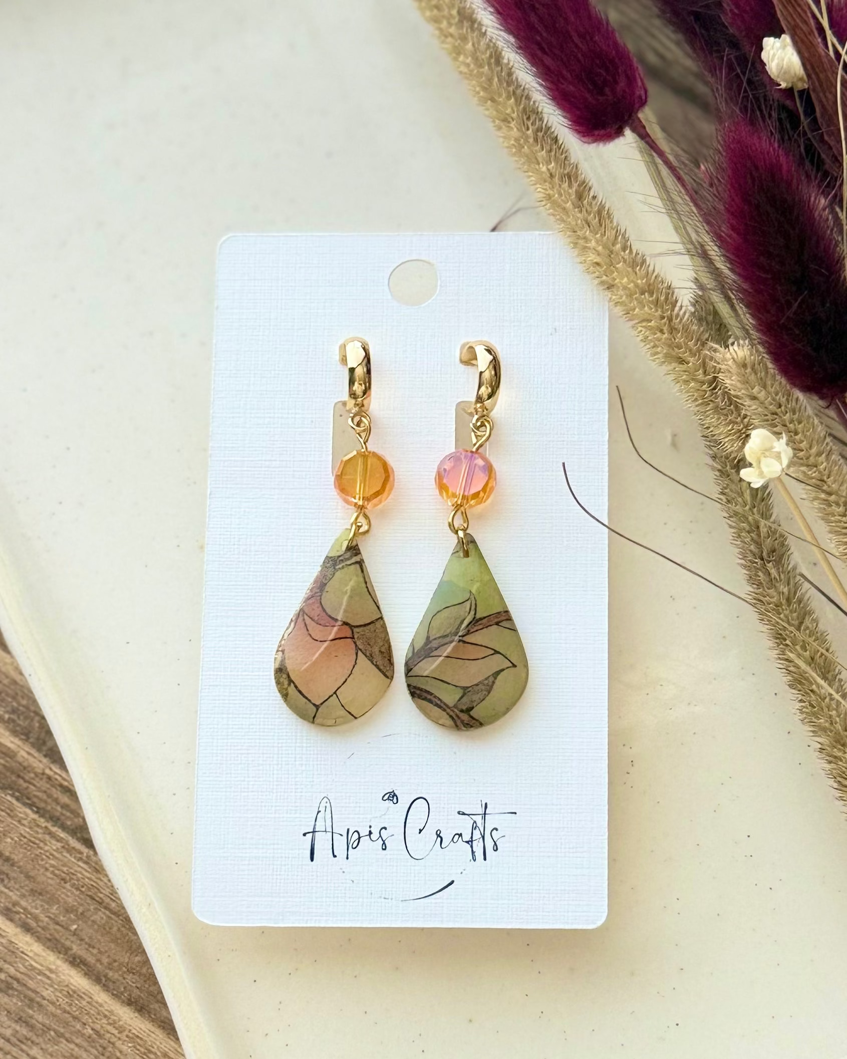 A pair of teardrop-shaped drop earrings with gold-tone hooks and orange crysta, featuring marbled green, beige, and brown stained glass drops