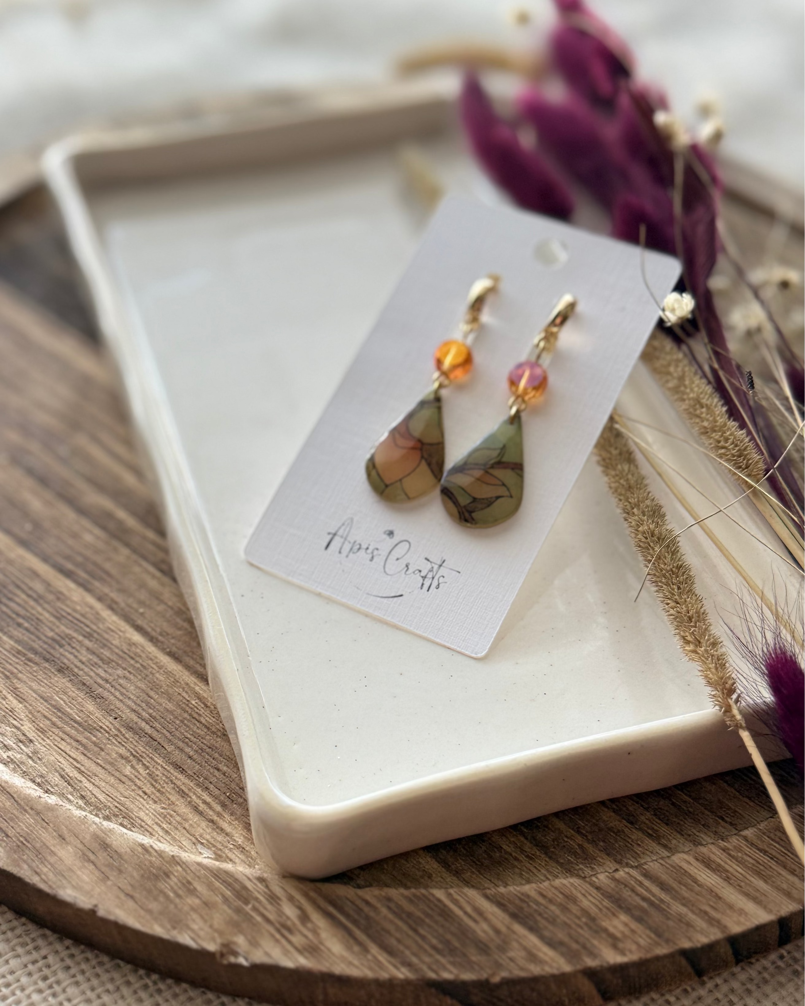 A pair of teardrop-shaped drop earrings with gold-tone hooks and orange crysta, featuring marbled green, beige, and brown stained glass drops