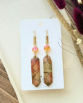 A pair of prism shaped dangling earrings with  translucent pink and yellow stained glass drop and an orange crystal accent.