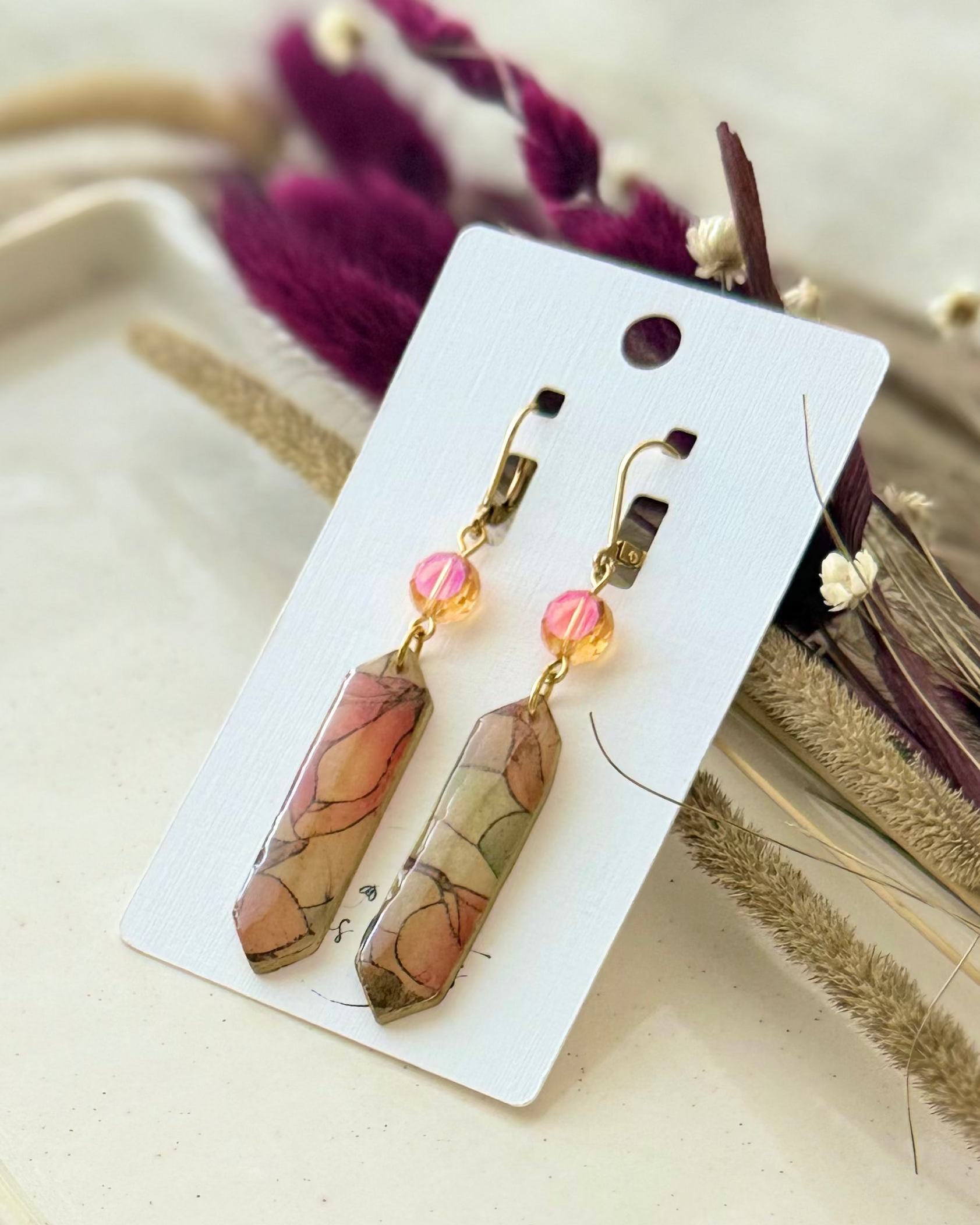 A pair of prism shaped dangling earrings with  translucent pink and yellow stained glass drop and an orange crystal accent.