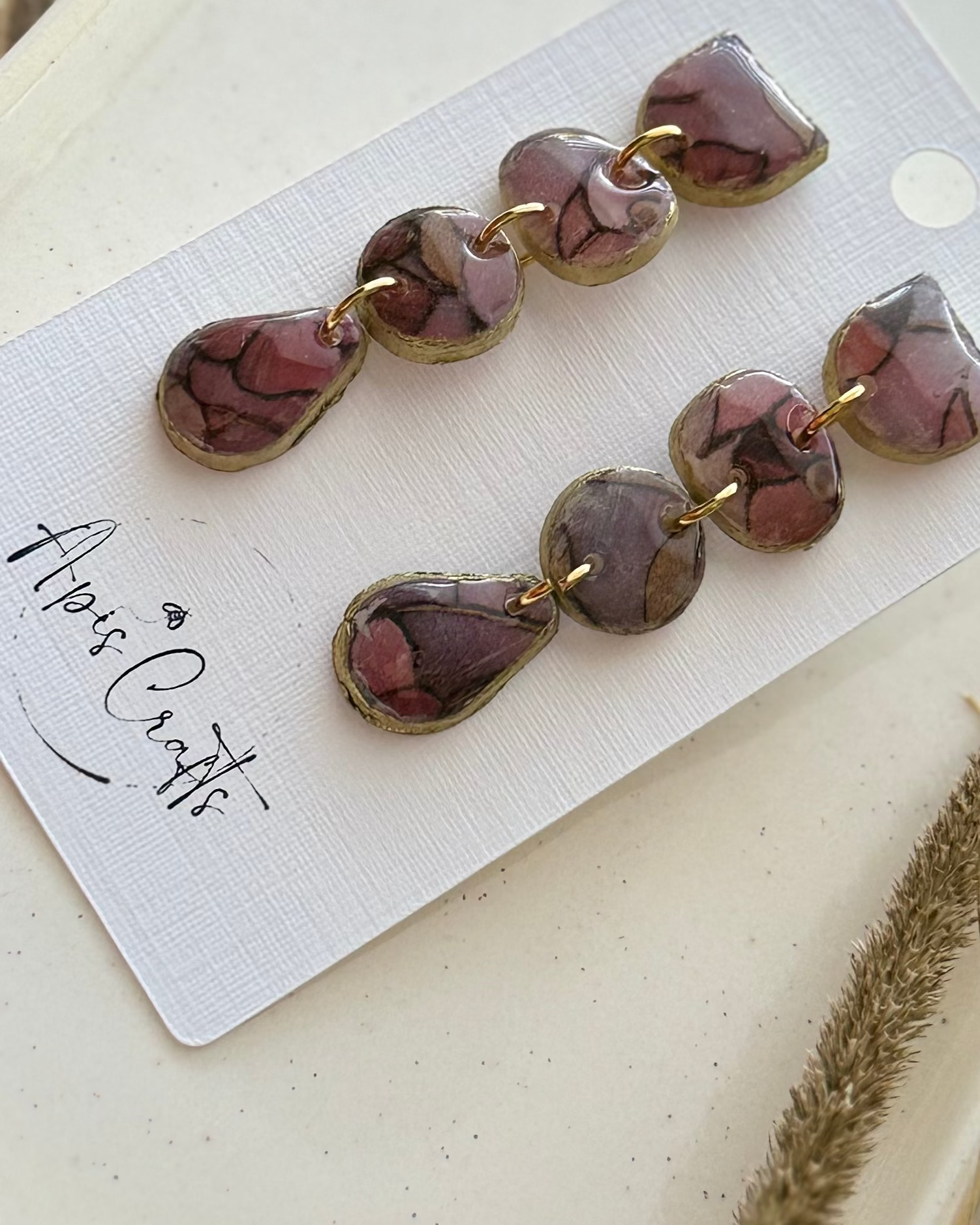 A pair of dangling earrings with three stacked oval beads in a dusty mauve-brown marbled pattern and gold-tone settings