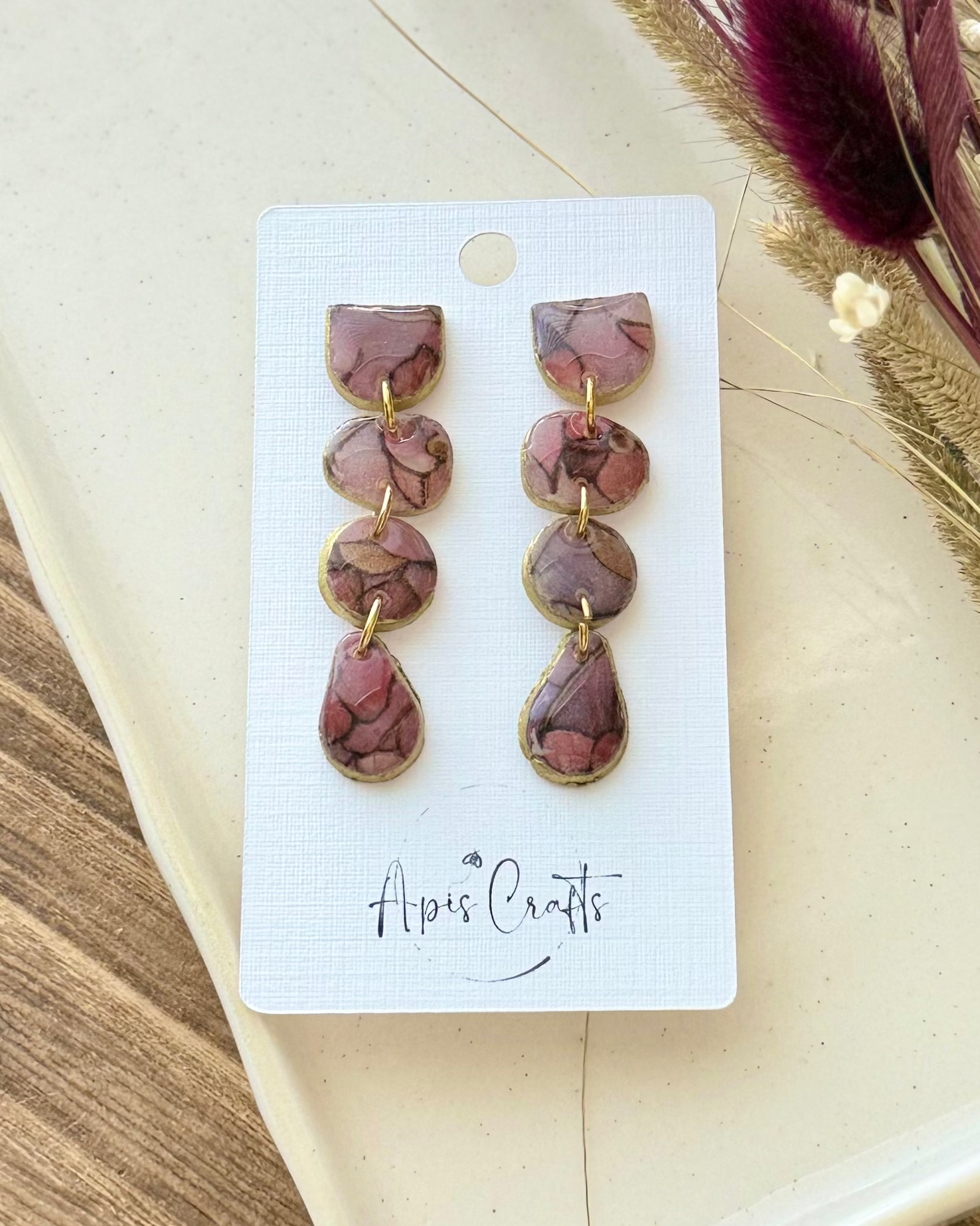 A pair of dangling earrings with three stacked oval beads in a dusty mauve-brown marbled pattern and gold-tone settings