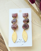 A pair of dangling earrings with three stacked oval beads in a dusty mauve-brown marbled pattern and gold-tone settings