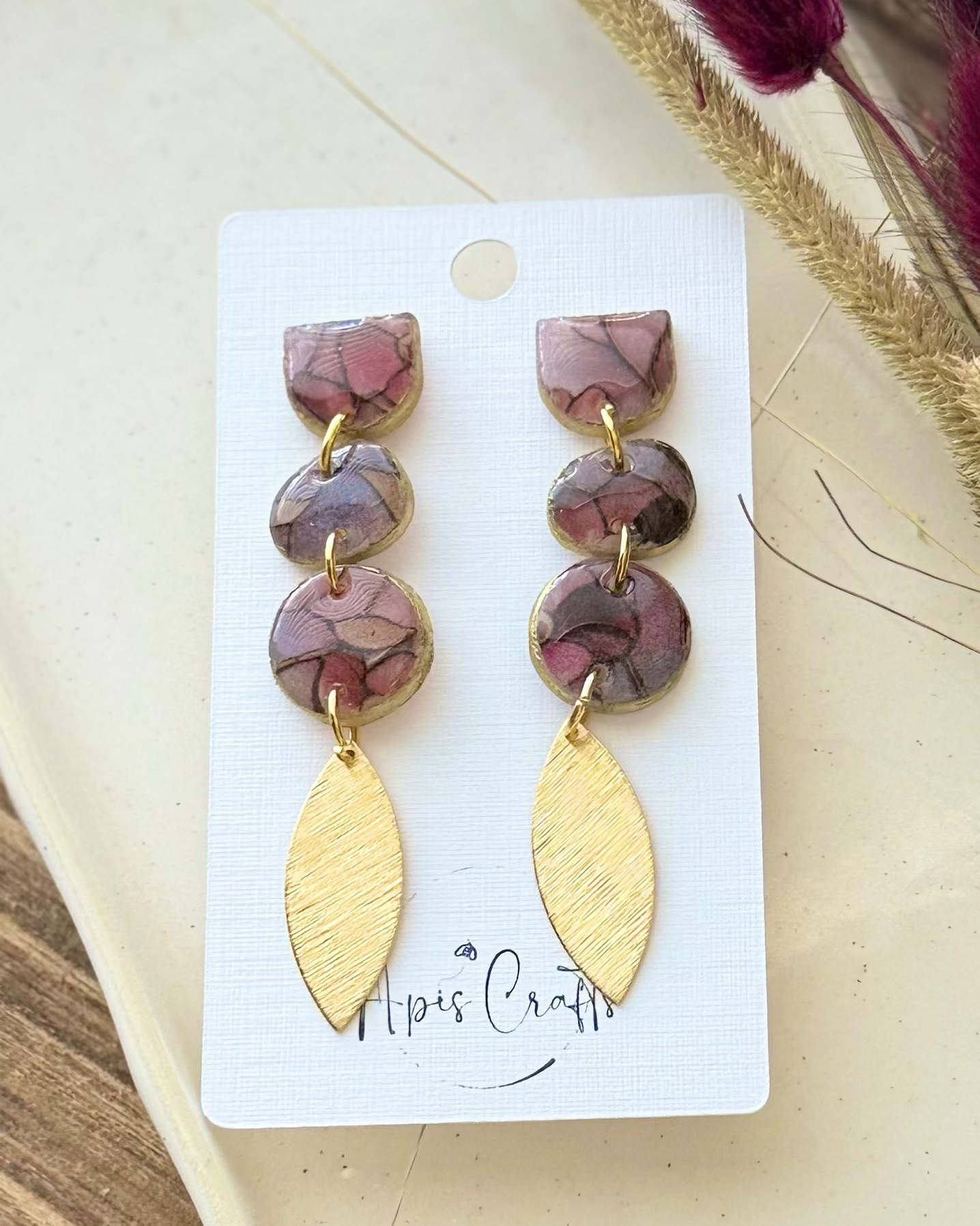 A pair of dangling earrings with three stacked oval beads in a dusty mauve-brown marbled pattern and gold-tone settings