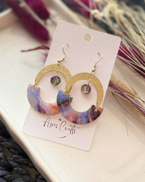 A pair of gold-tone hoop earrings with semi-circular marbled inserts in purple, blue, and pink