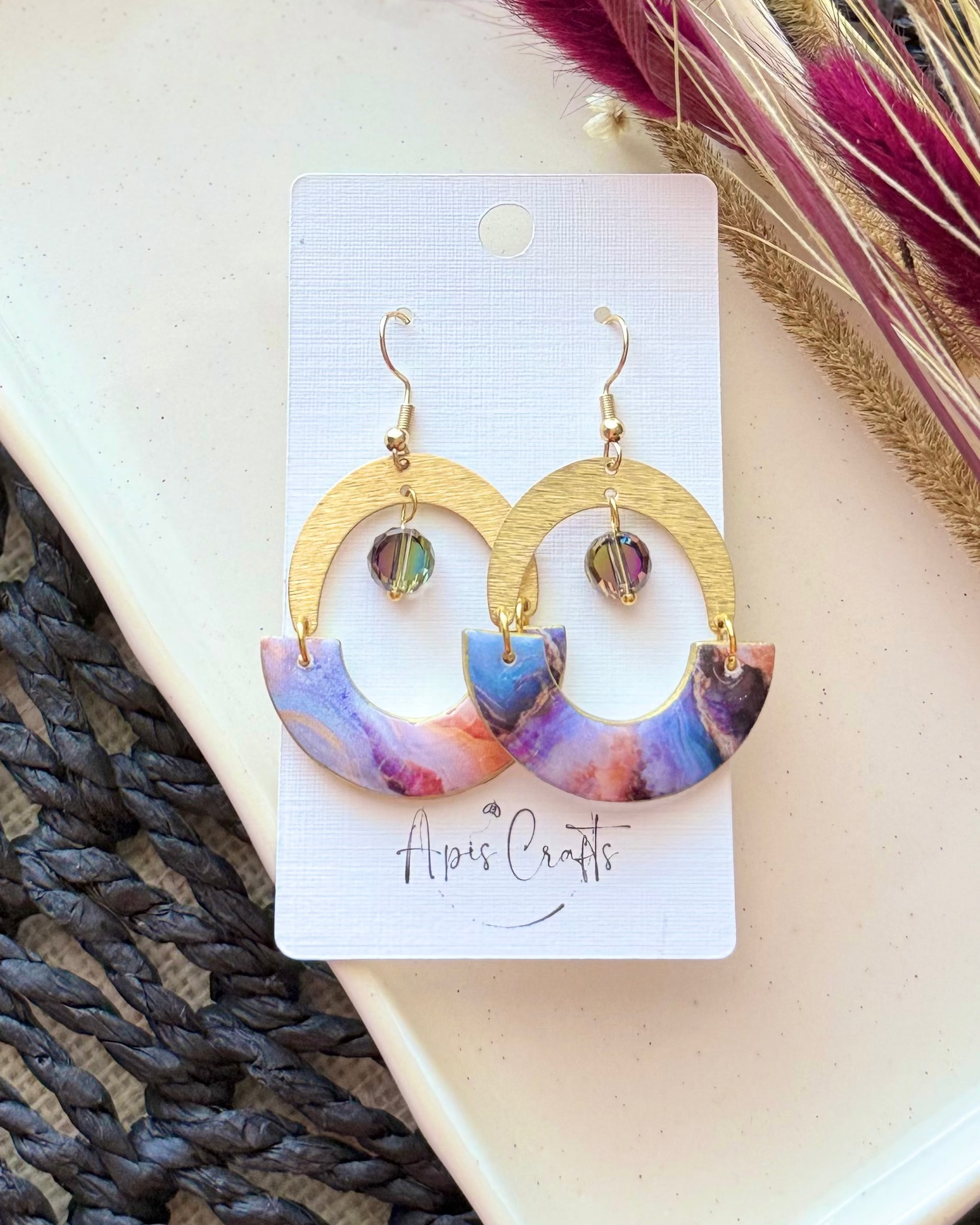 A pair of gold-tone hoop earrings with semi-circular marbled inserts in purple, blue, and pink