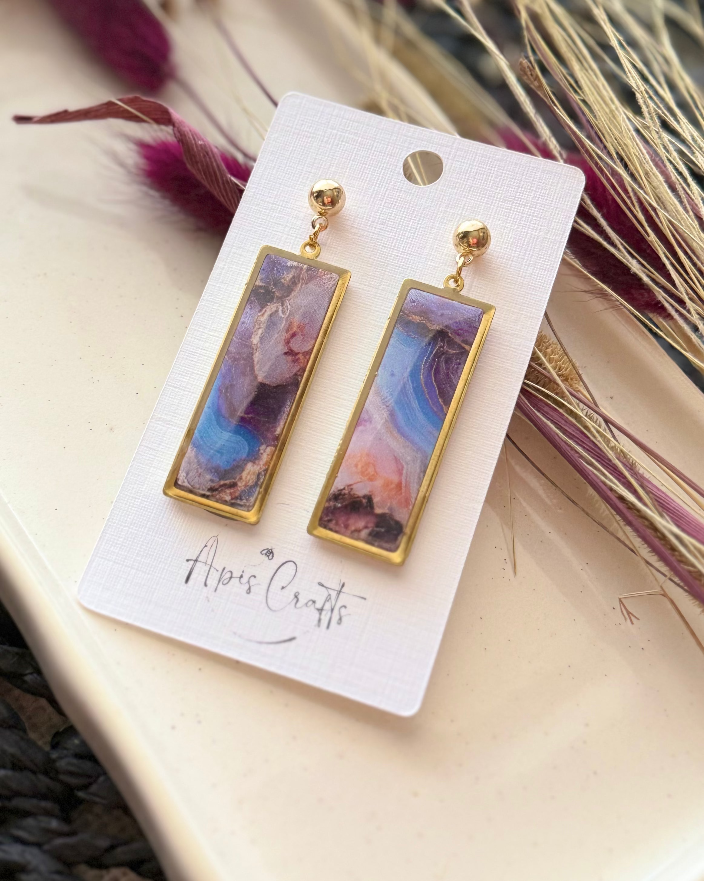 A pair of gold-tone drop earrings with rectangular marbled pendants in purple, blue, pink, and white