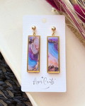 A pair of gold-tone drop earrings with rectangular marbled pendants in purple, blue, pink, and white