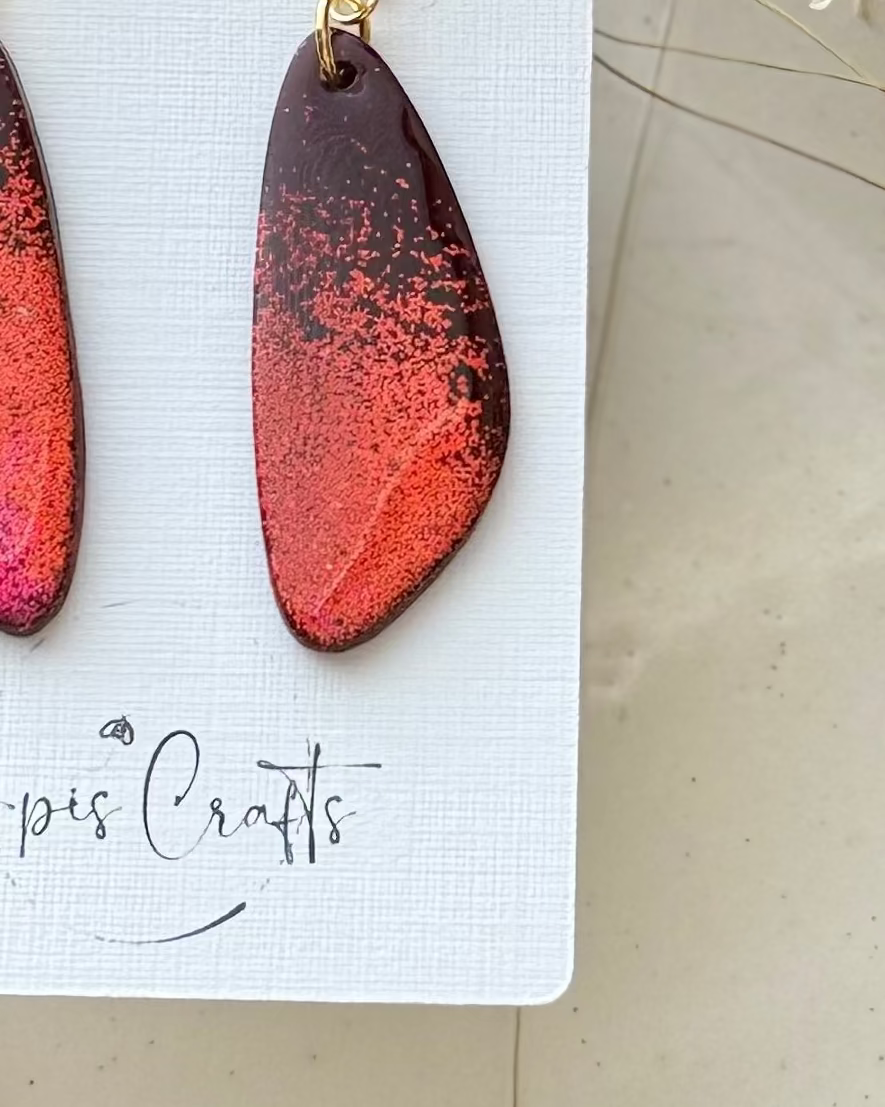 A pair of teardrop-shaped drop earrings with gold semicircle studs and a red ombré glitter body
