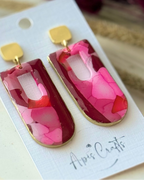 A pair of statement earrings with rectangular ppendants filled with layered pink and red faux stone design, attached to gold square studs