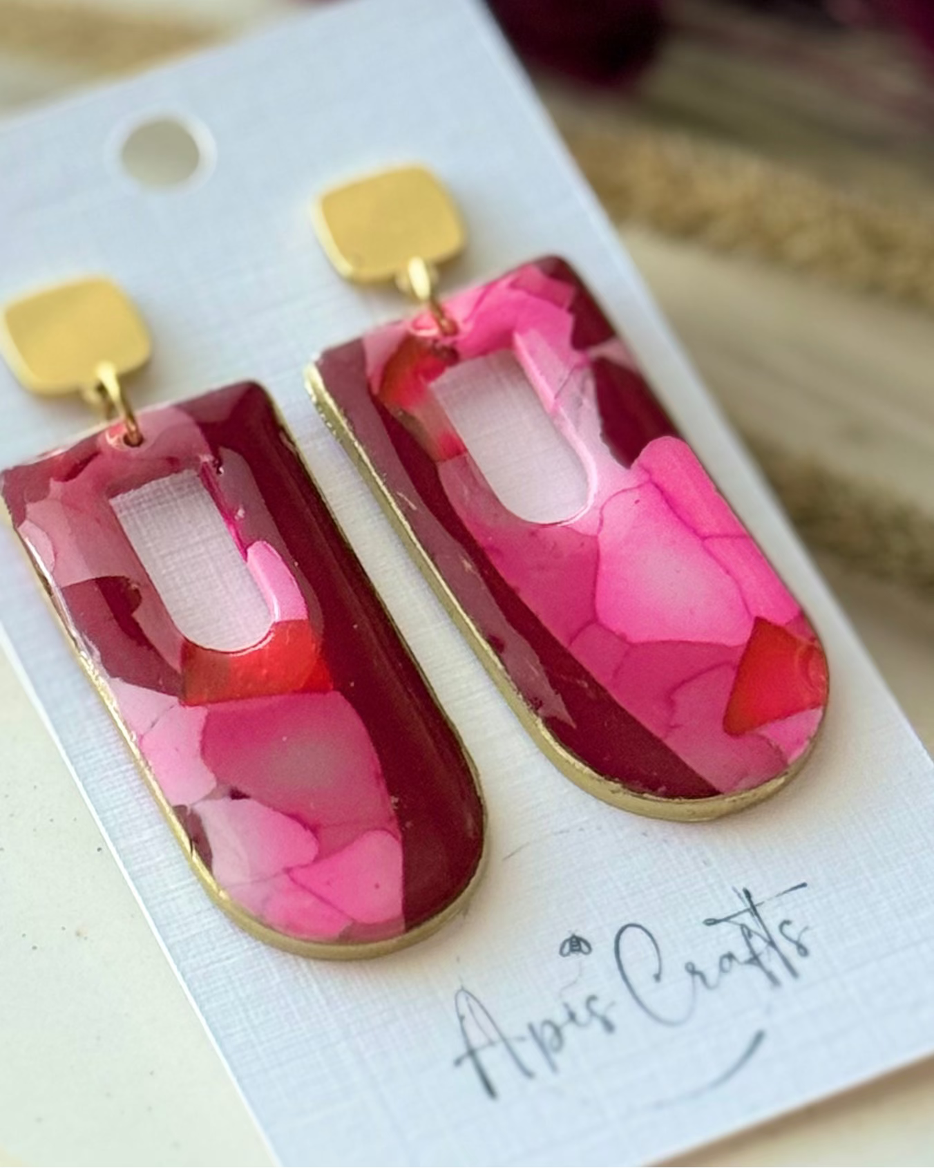 A pair of statement earrings with rectangular ppendants filled with layered pink and red faux stone design, attached to gold square studs