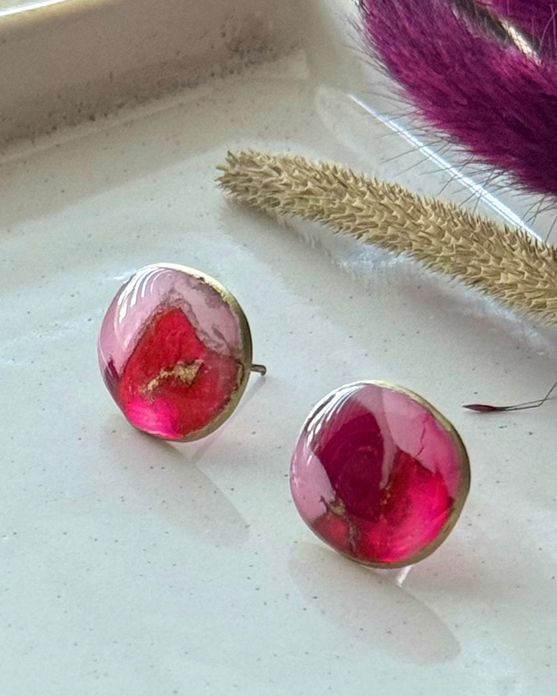 A pair of pebble shaped stud earrings with oval pink and red faux stone finish