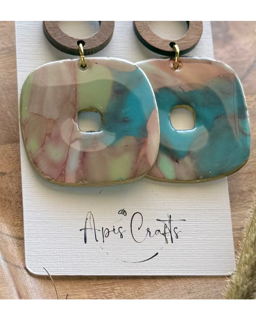 A pair of drop earrings with a round wooden hoop and a marbled square pendant in pink, turquoise blue, and pale green.
