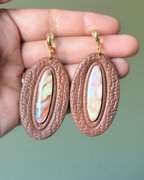 A pair of oval drop earrings with textured dark brown outer rings and marbled pastel inlay center
