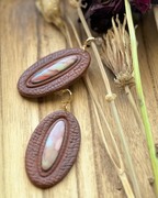 A pair of oval drop earrings with textured dark brown outer rings and marbled pastel inlay center