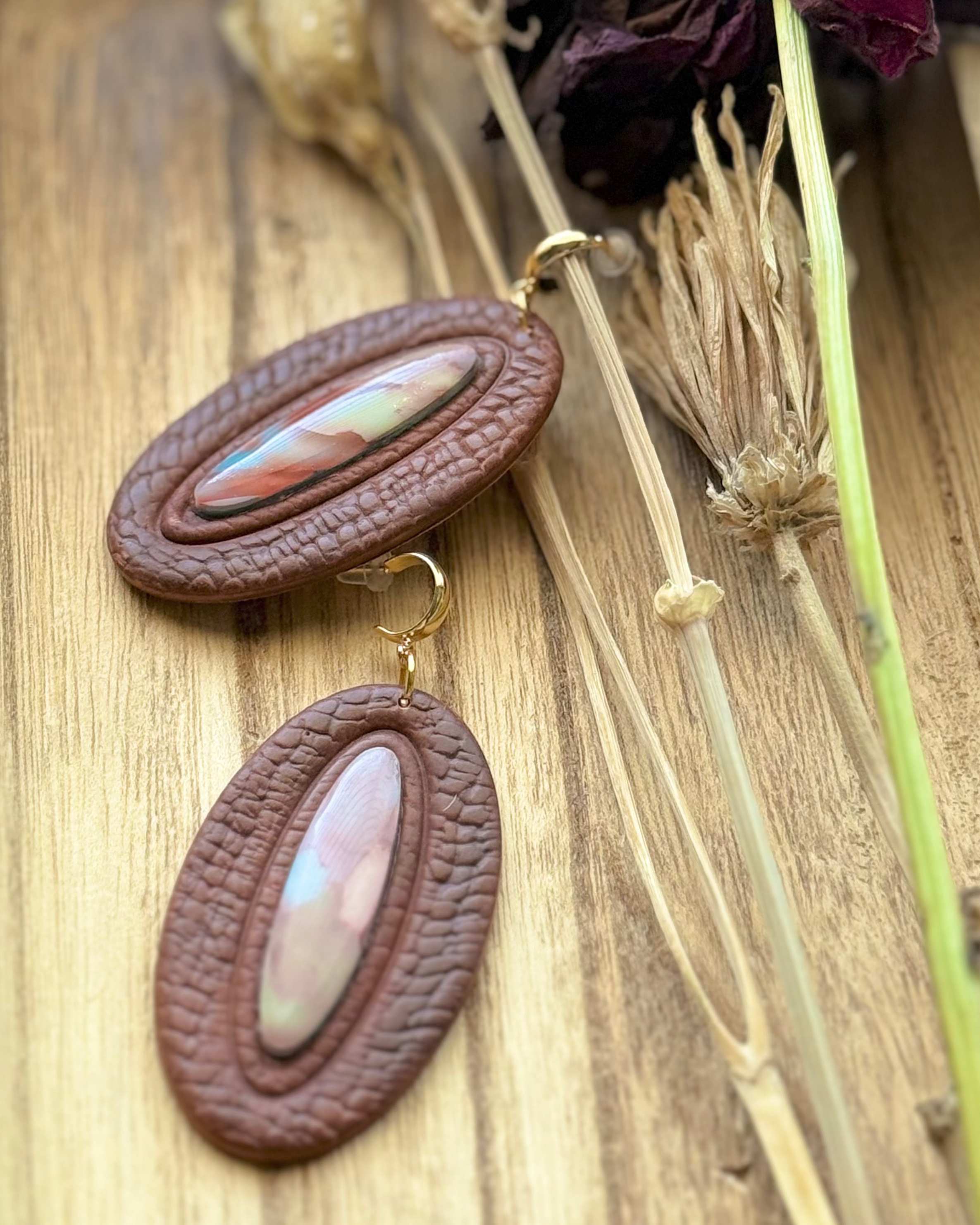A pair of oval drop earrings with textured dark brown outer rings and marbled pastel inlay center