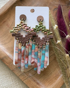 A pair of handmade statement earrings featuring textured gold and green top pieces, brown geometric middle bands, and dangling marbled fringe in pink, blue, and white.