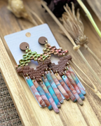 A pair of handmade statement earrings featuring textured gold and green top pieces, brown geometric middle bands, and dangling marbled fringe in pink, blue, and white.