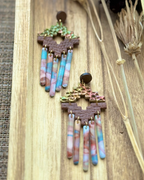 A pair of handmade statement earrings featuring textured gold and green top pieces, brown geometric middle bands, and dangling marbled fringe in pink, blue, and white.
