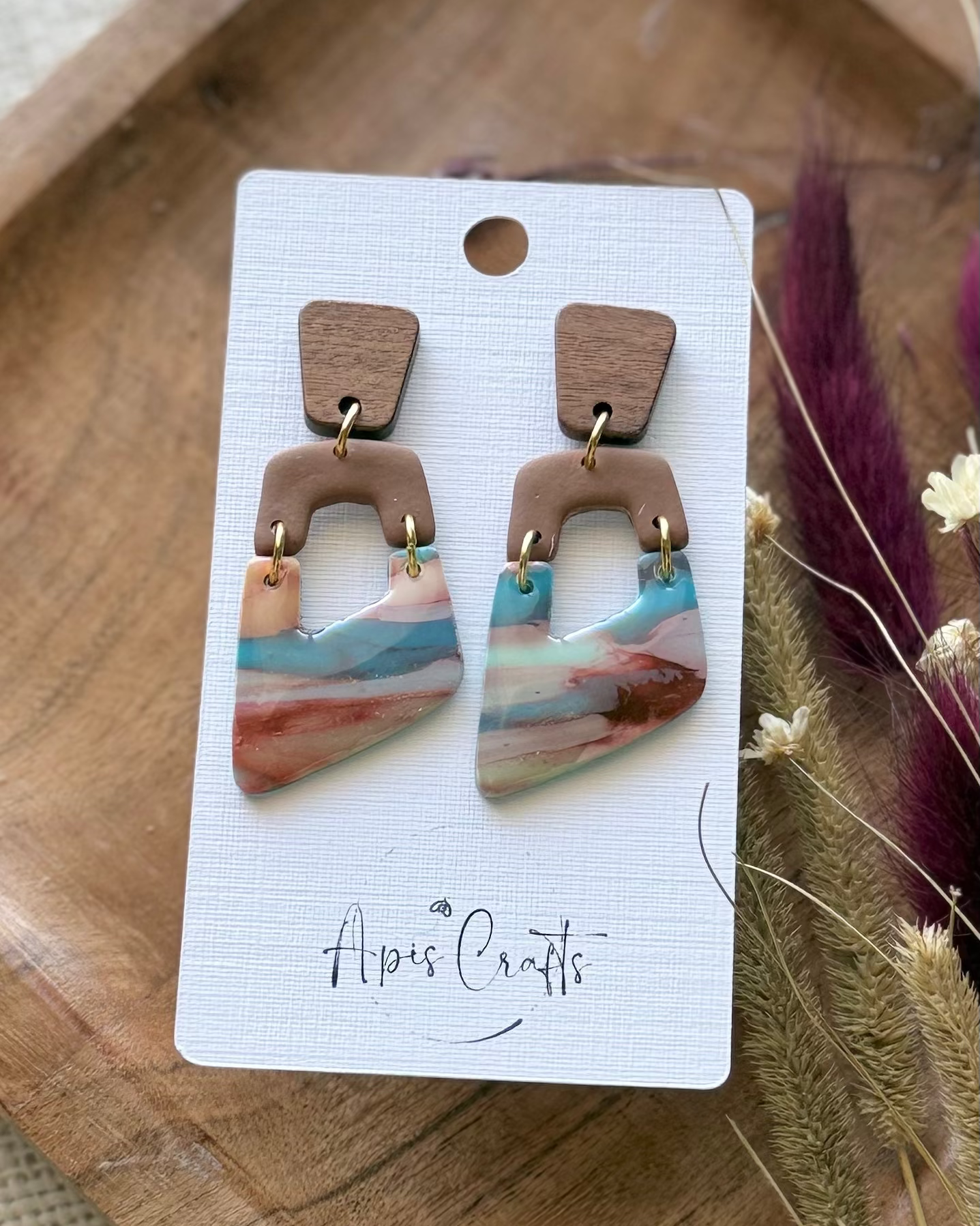 A pair of geometric dangle earrings with a light brown top section and a marbled lower section with pink, blue, and white tones