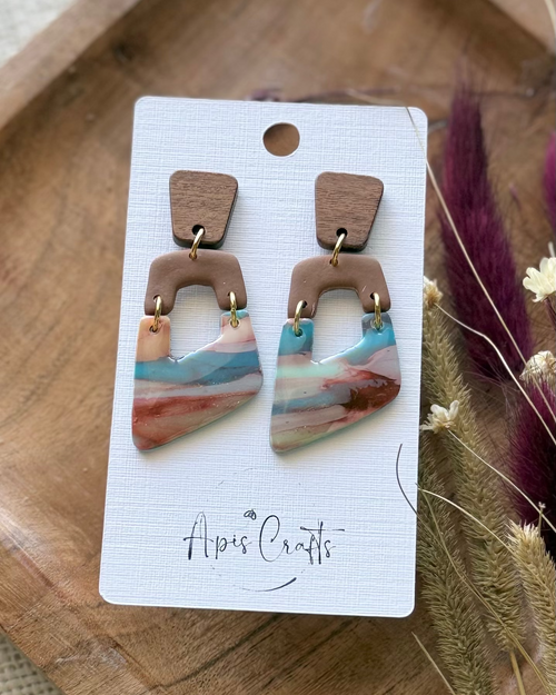 A pair of geometric dangle earrings with a light brown top section and a marbled lower section with pink, blue, and white tones