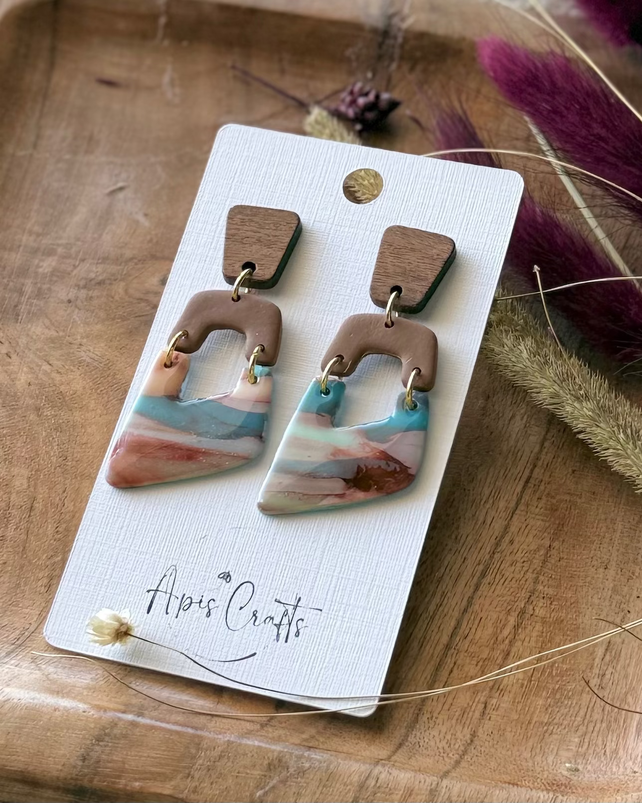 A pair of geometric dangle earrings with a light brown top section and a marbled lower section with pink, blue, and white tones