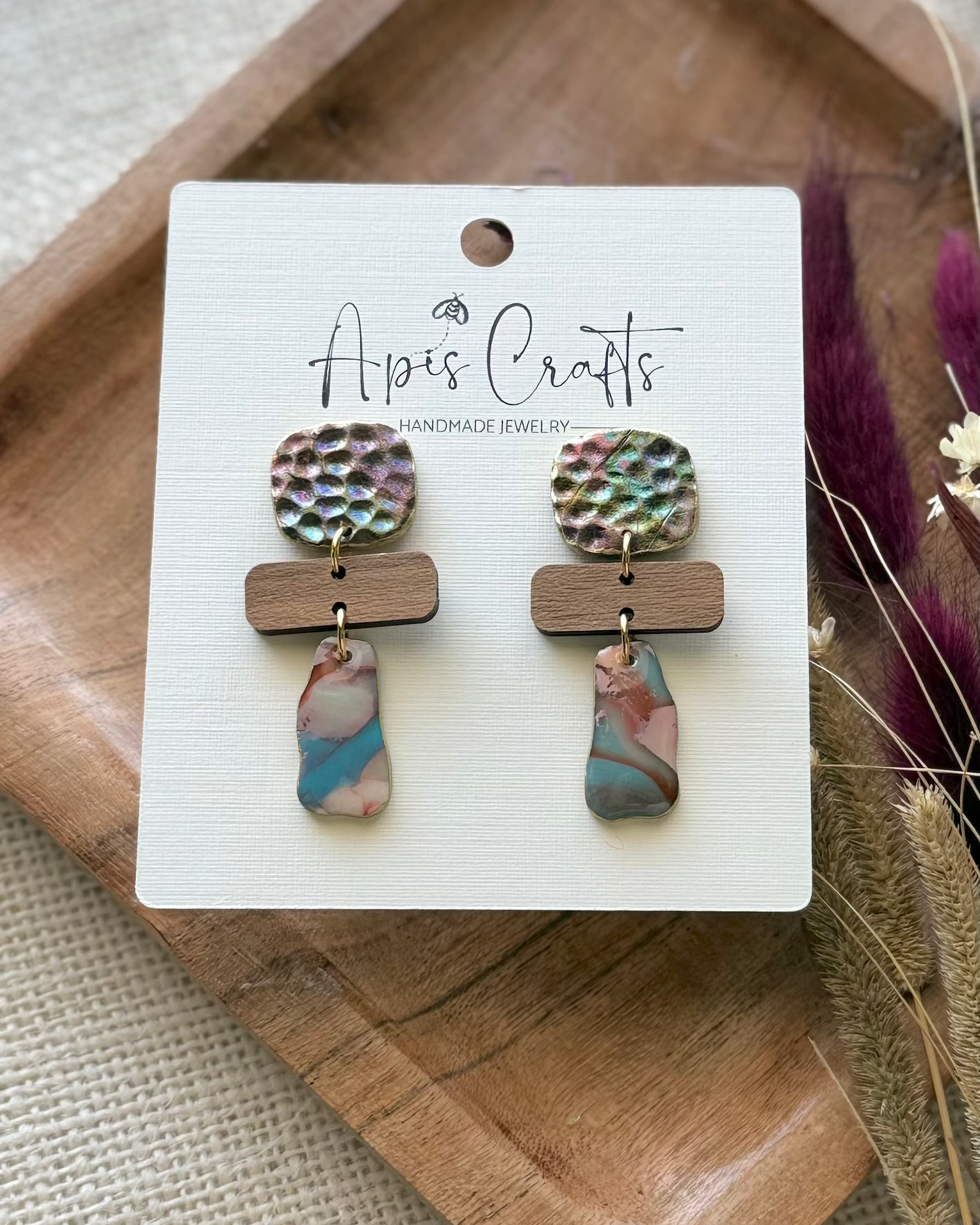 A pair of handmade dangle earrings with textured drops and a dangling marbled bottom piece in blue, pink, and cream.