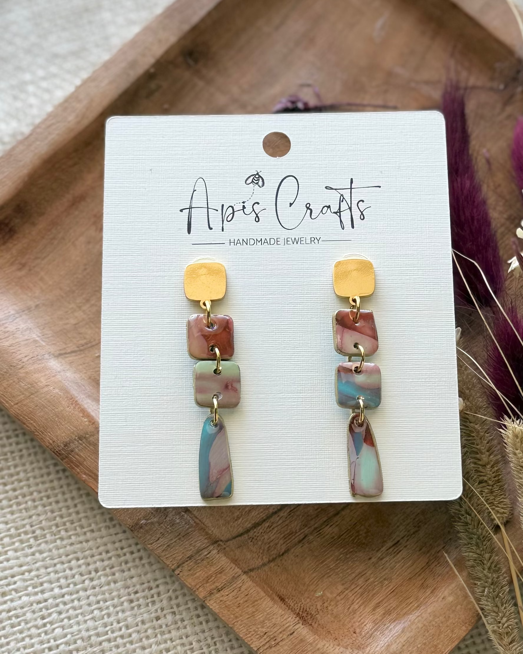A pair of handmade dangle earrings with textured drops and a dangling marbled bottom piece in blue, pink, and cream.