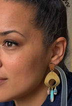 A close-up of a woman wearing a large gold-toned statement earring with turquoise and white dangling accents.