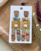 A pair of bohemian-style drop earrings featuring a brown wood-grain top, gold-tone hammered square links, and marbled drops in pink, blue, and green.