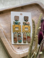 A pair of bohemian-style drop earrings featuring a brown wood-grain top, gold-tone hammered square links, and marbled drops in pink, blue, and green.