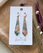 A pair of dangling earrings with marbled pendants in teal, pink, and beige, hanging from gold-tone hoops