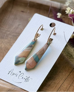 A pair of dangling earrings with marbled pendants in teal, pink, and beige, hanging from gold-tone hoops