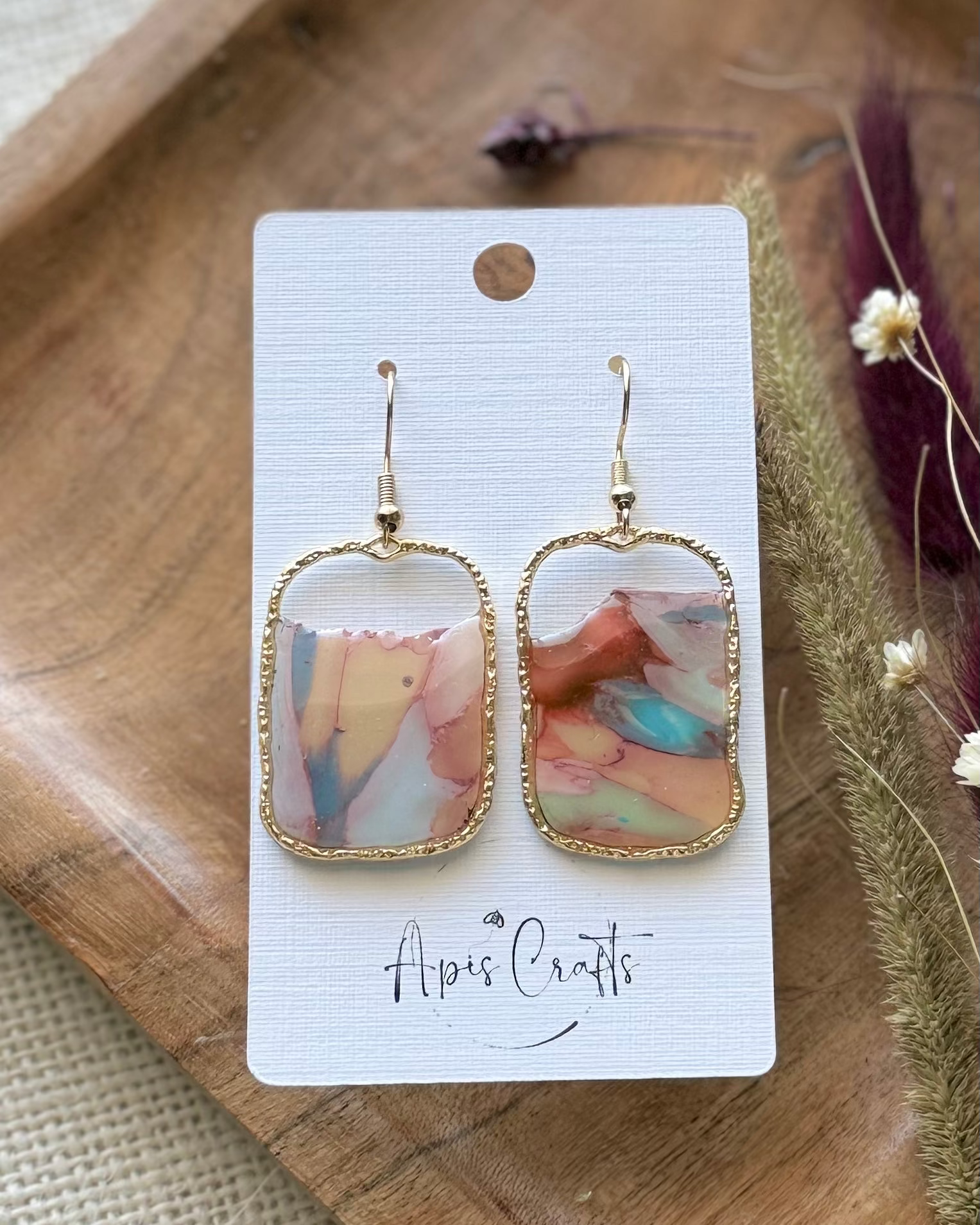 A pair of gold-tone drop earrings with rectangular marbled pendants in soft pastel tones