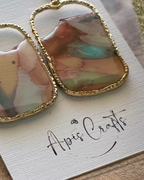 A pair of gold-tone drop earrings with rectangular marbled pendants in soft pastel tones