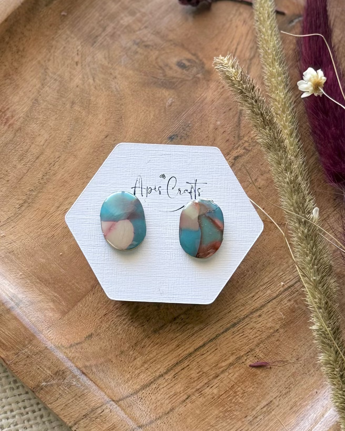 A pair of oval stud earrings with a marbled pattern of teal, pink, and cream