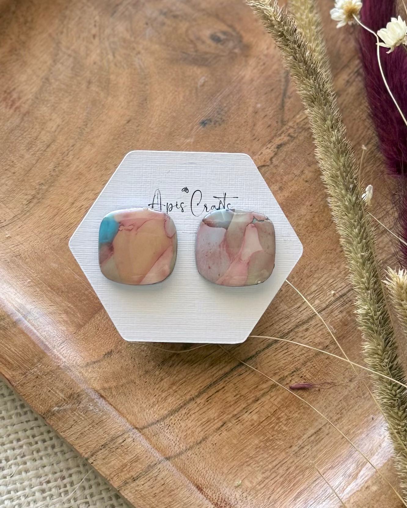 A pair of square stud earrings with a pink, peach, and light blue marbled pattern