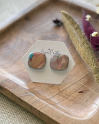 A pair of square stud earrings with a pink, peach, and light blue marbled pattern