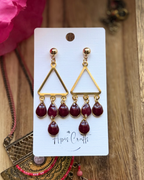 A pair of gold triangle dangle earrings with five deep burgundy teardrop beads hanging from each earring