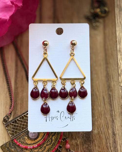 A pair of gold triangle dangle earrings with five deep burgundy teardrop beads hanging from each earring