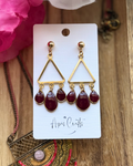A pair of gold triangle dangle earrings with three deep burgundy teardrop beads hanging from each earring