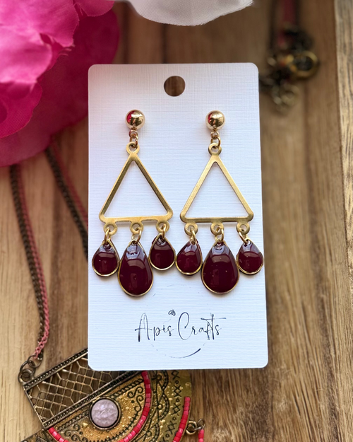 A pair of gold triangle dangle earrings with three deep burgundy teardrop beads hanging from each earring